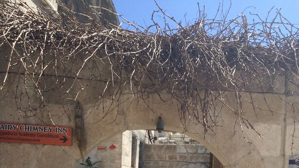 An arched stone entrance with a sign for Fairy Chimney Inn. There are potted plants and a bell above the archway. - Fairy Chimney Inn (Nevsehir)