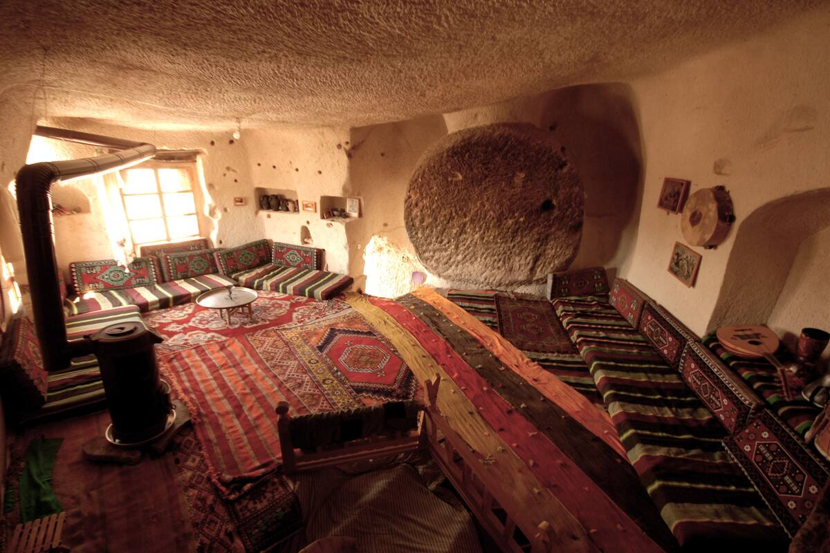 A traditional room with a large stone wall, a wooden sofa set, and a patterned rug.