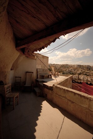 A rustic room with a wooden ceiling, a large window overlooking a rocky landscape, and a simple seating area with a chair and a table.