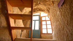 A rustic stone interior with a wooden ladder, a blue door, and a window with sunlight streaming through. - Fairy Chimney Inn (Nevsehir)
