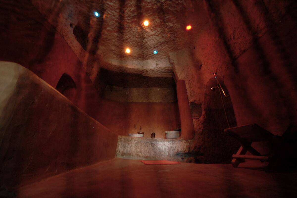 A dimly lit interior with a stone wall, a raised platform with pots, and a wooden chair.