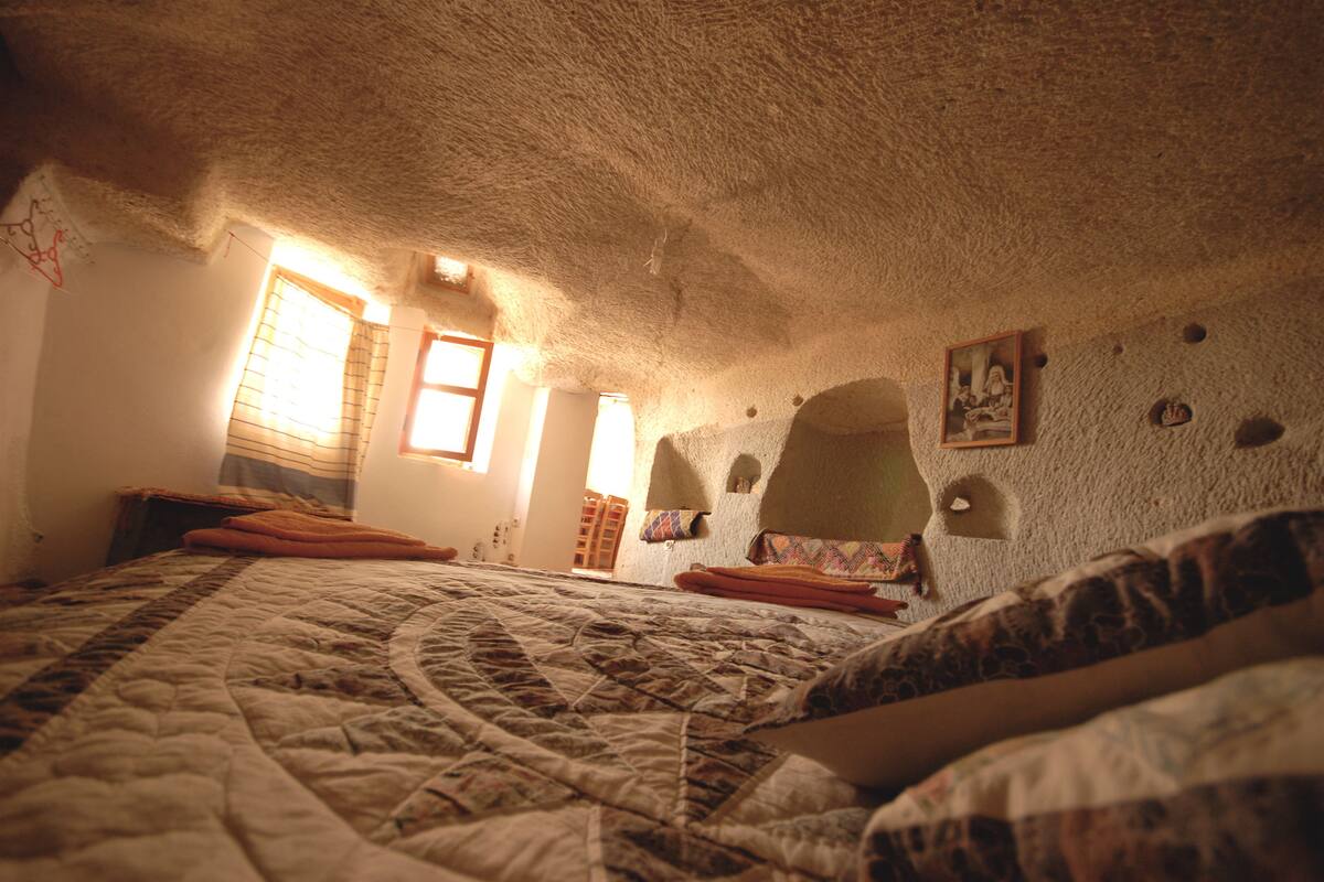A bedroom with a large bed, a window with blinds, and a textured ceiling.
