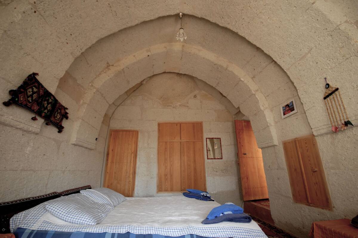 A room with a high arched ceiling, wooden doors, a bed with blue and white bedding, and a small framed picture on the wall.