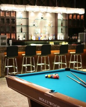 A pool table with a 'HOLLYWOOD' label, a bar area with stools, and a bar stocked with bottles.