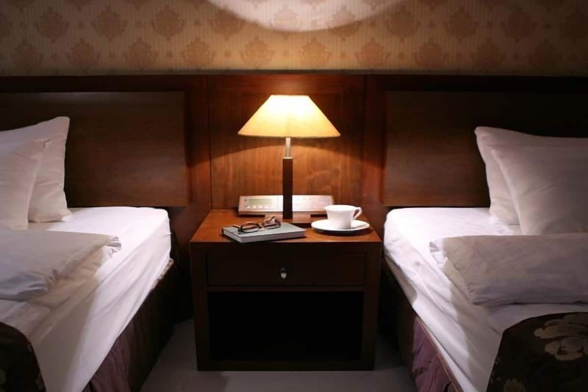 A hotel room with two single beds, a nightstand with a lamp, a cup, and a book.