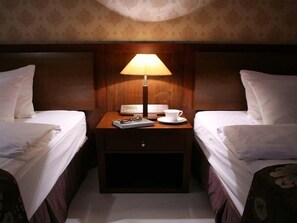 A hotel room with two single beds, a nightstand with a lamp, a cup, and a book.