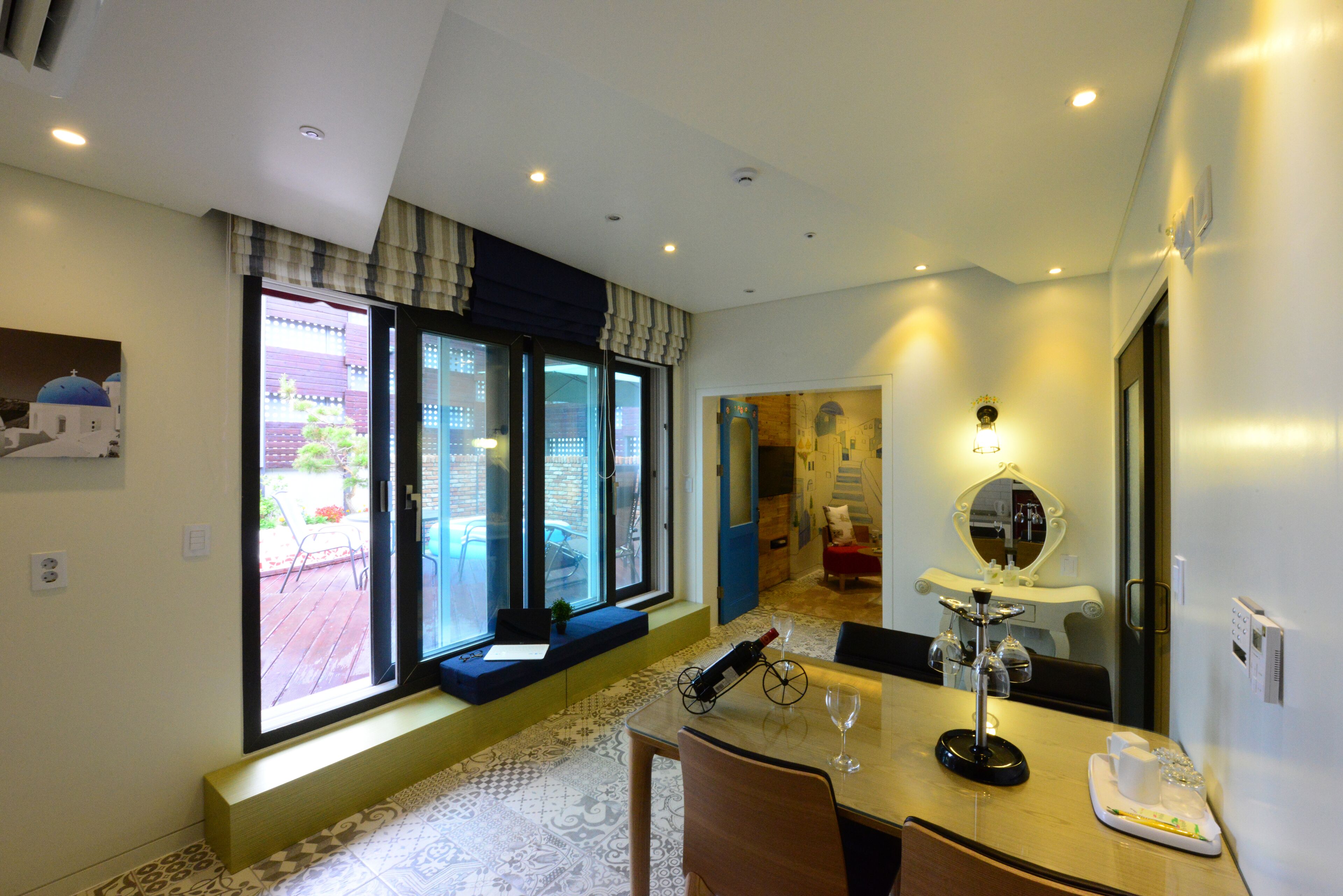 A hotel room with a large window, a dining table with chairs, a small sofa, and a mirror.