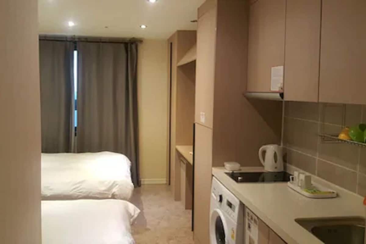 A hotel room with two beds, a washing machine, and a kitchenette with a coffee maker and fruit.