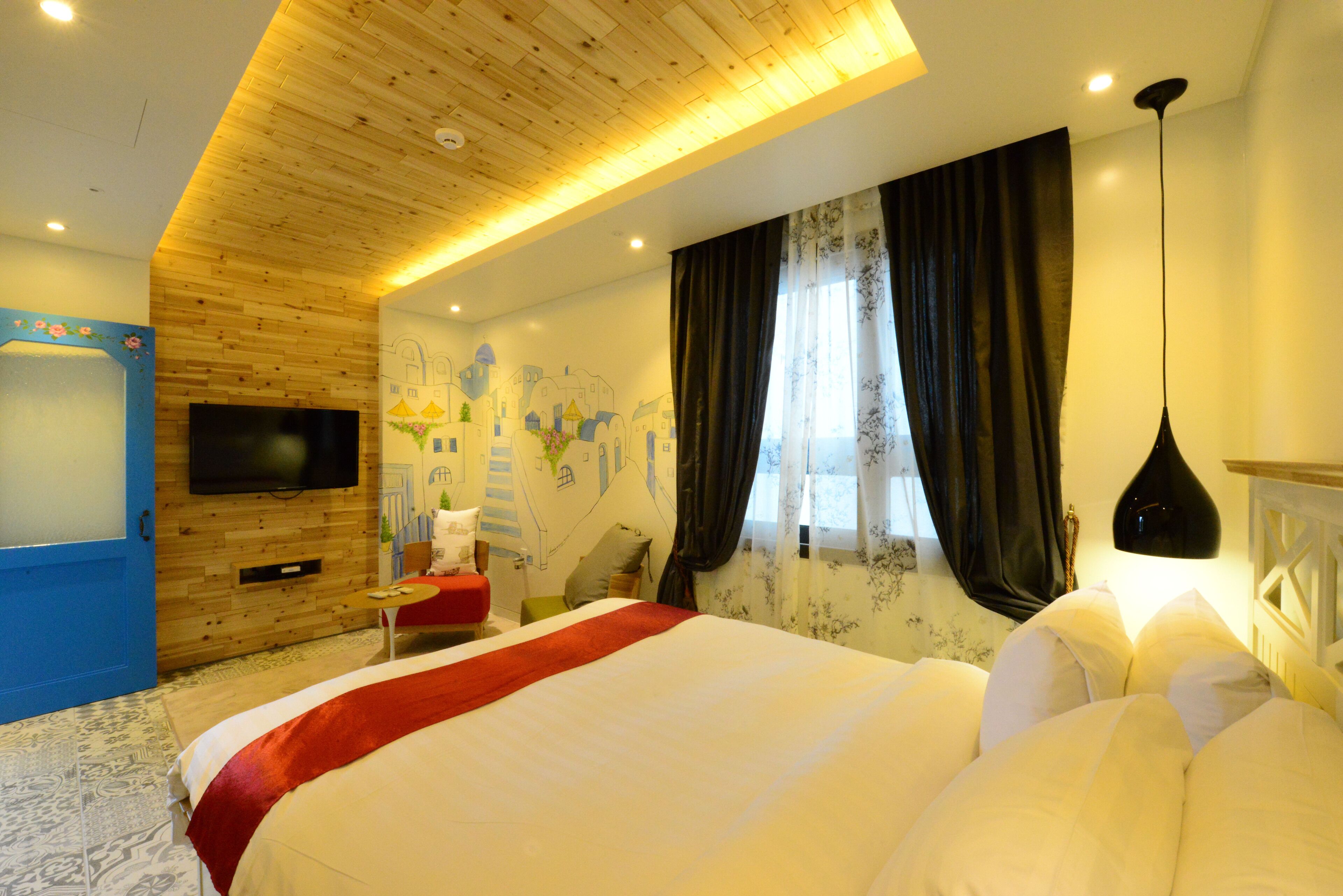 Une chambre d’hôtel avec un grand lit, un téléviseur à écran plat fixé au mur, un plafond en bois et une fenêtre avec des rideaux.