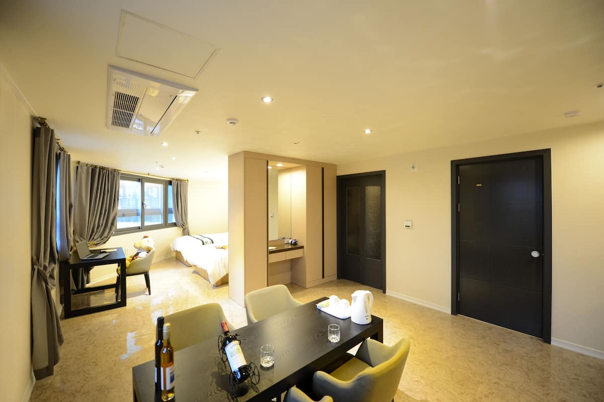 A hotel room with a dining area, a bed, a desk with a laptop, a teddy bear, and a minibar.