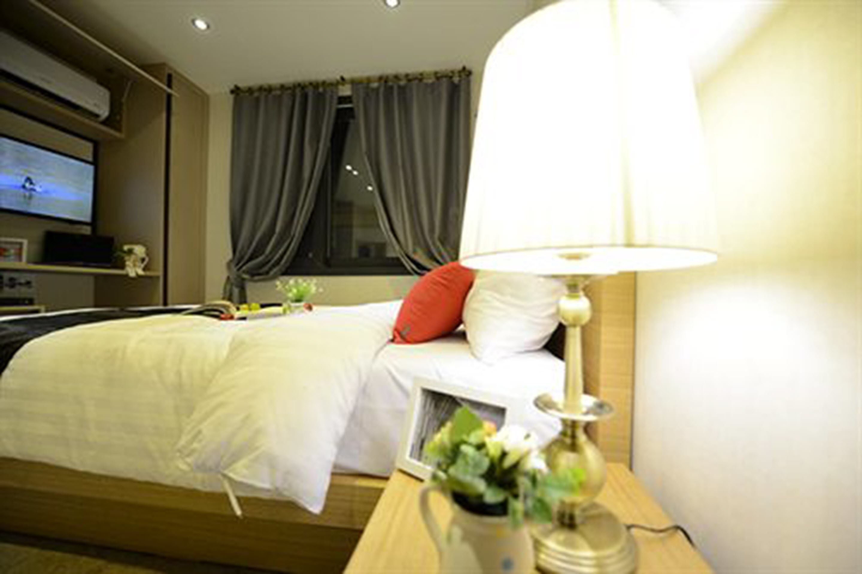 A hotel room with a bed, a bedside lamp, a TV on the wall, and a window with curtains.