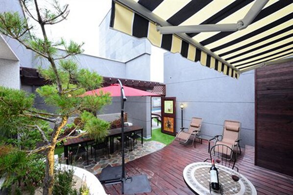 Un patio con mesa y sillas, rodeado de follaje y una terraza de madera.