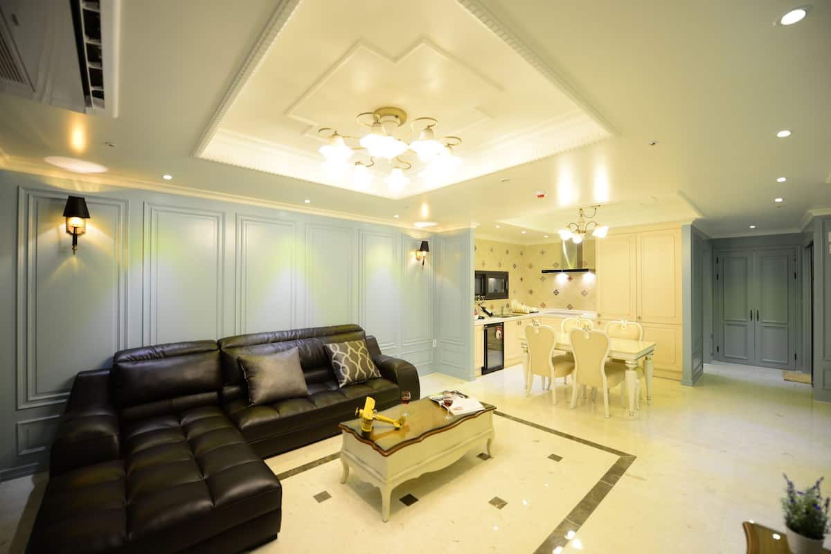 A modern living room with a black leather sofa, a wooden coffee table, and a dining area with white chairs.