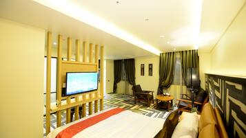 A hotel room with a large bed, a TV, a desk with a chair, and a small table.