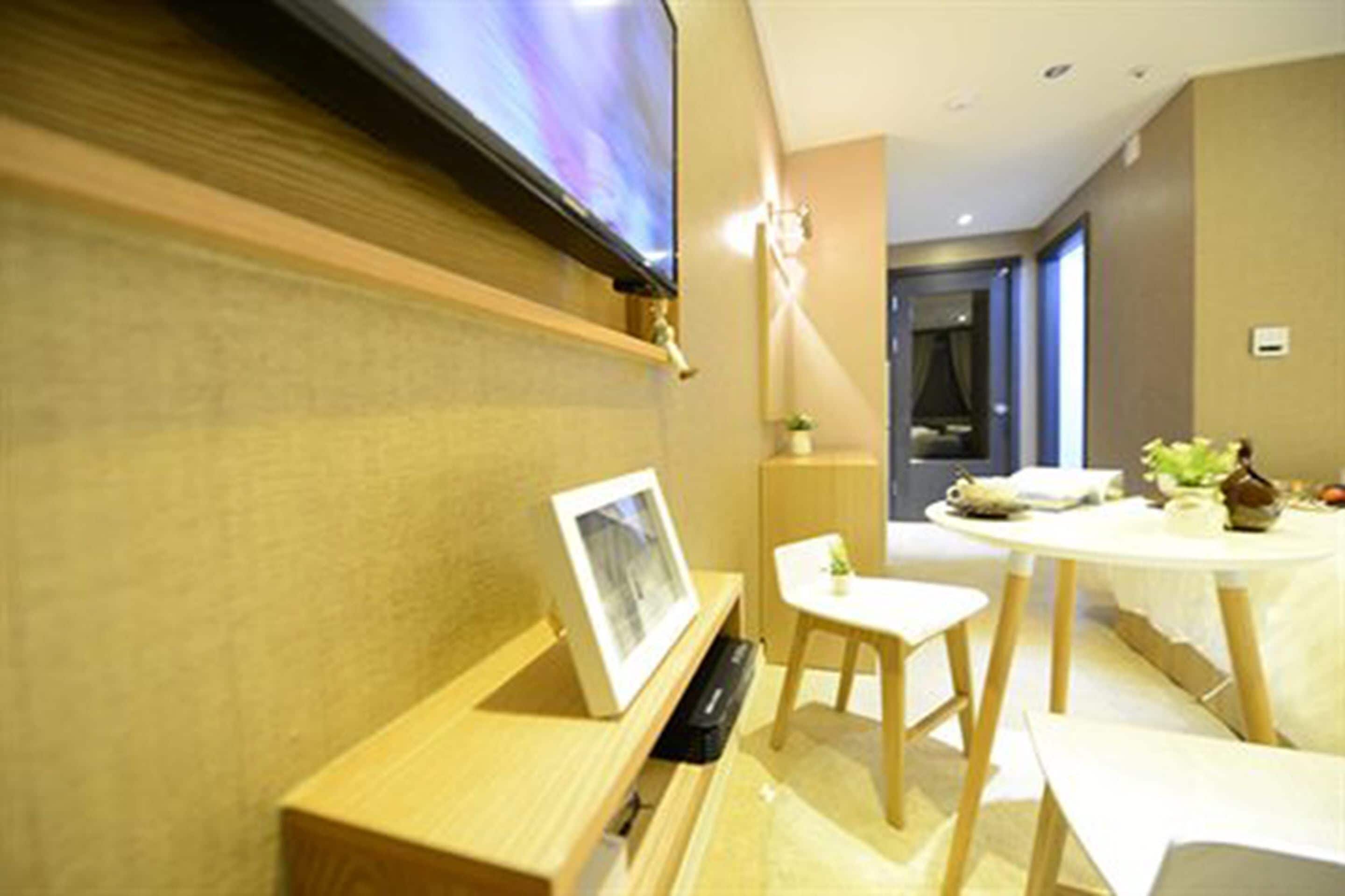 Una habitación de hotel moderna con un televisor de pantalla plana montado en la pared, una pequeña mesa con una silla y un marco de fotos sobre una mesita de noche de madera.