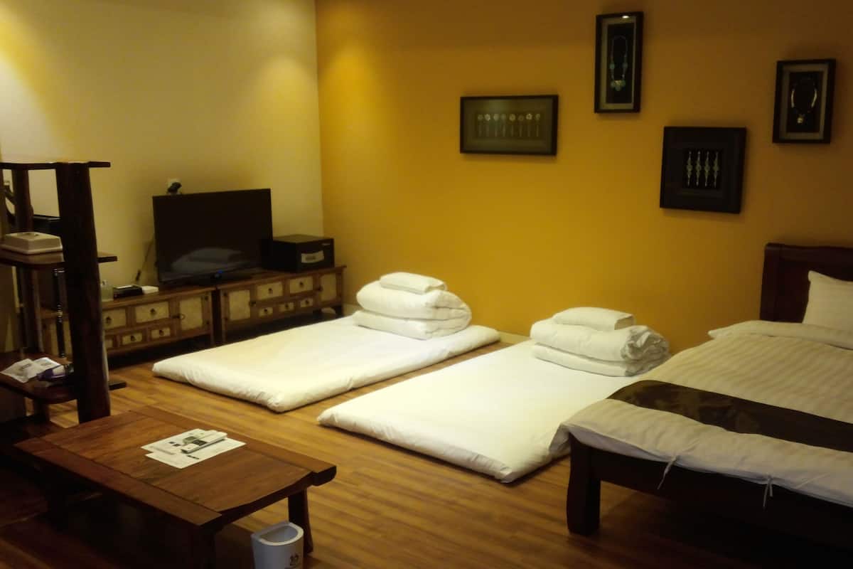 A hotel room with a bed, two white towels, a wooden nightstand, a television, and framed pictures on the wall.