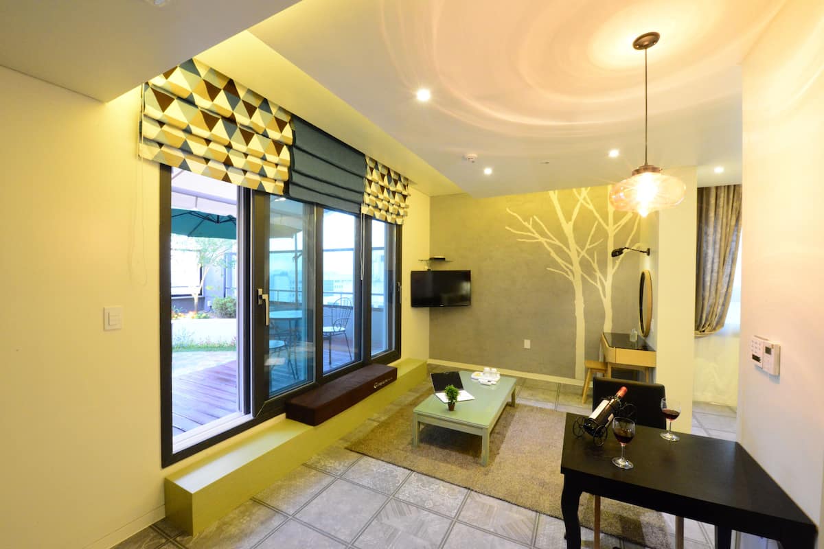 A modern living room with a large window, a flat-screen TV, a coffee table, and a dining table.