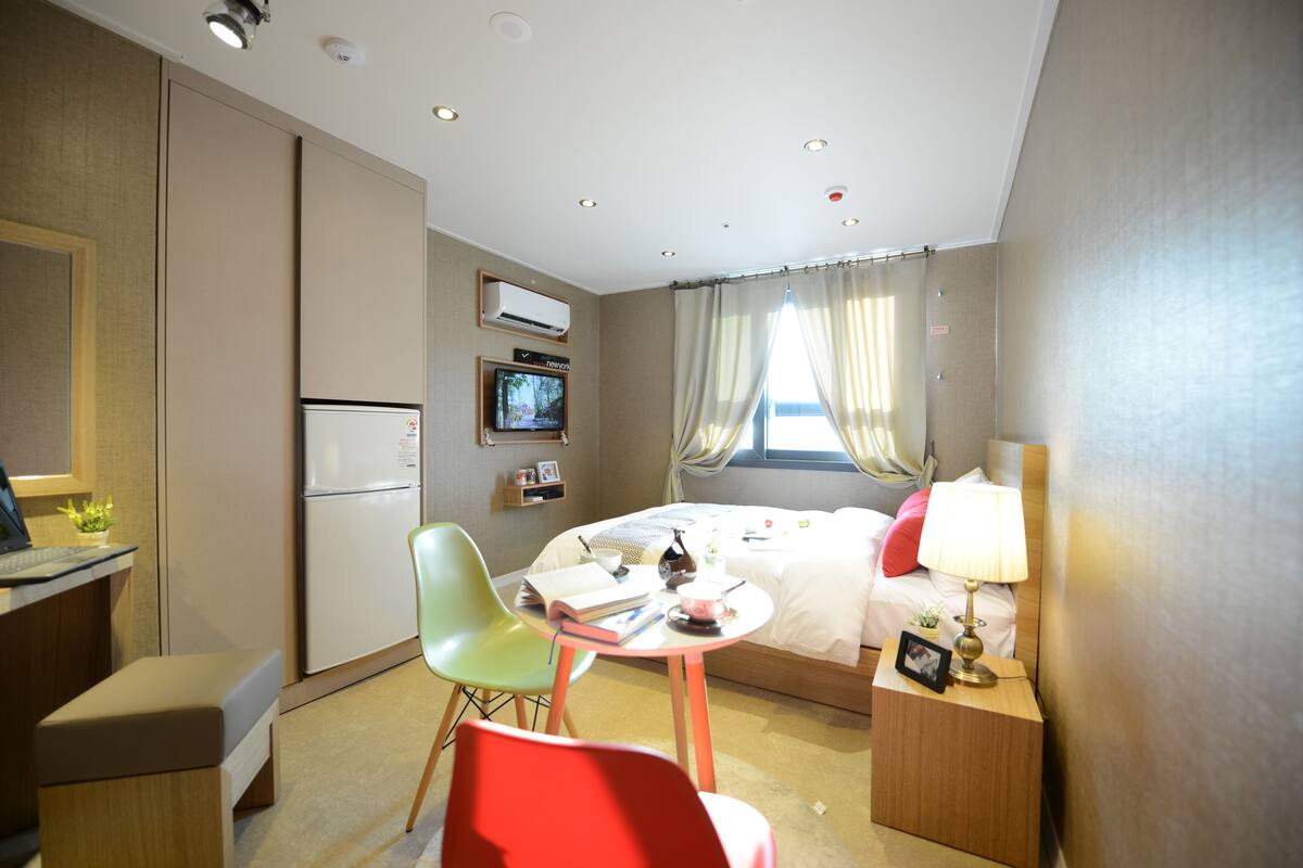 A hotel room with a bed, a desk, a chair, a small table, and a TV.
