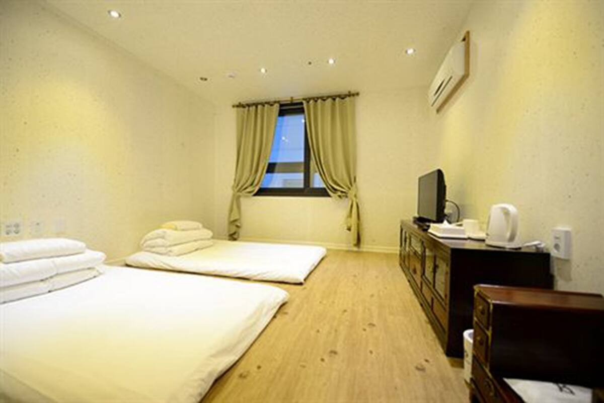 A room with two beds, a television, a dresser, and a window with curtains.