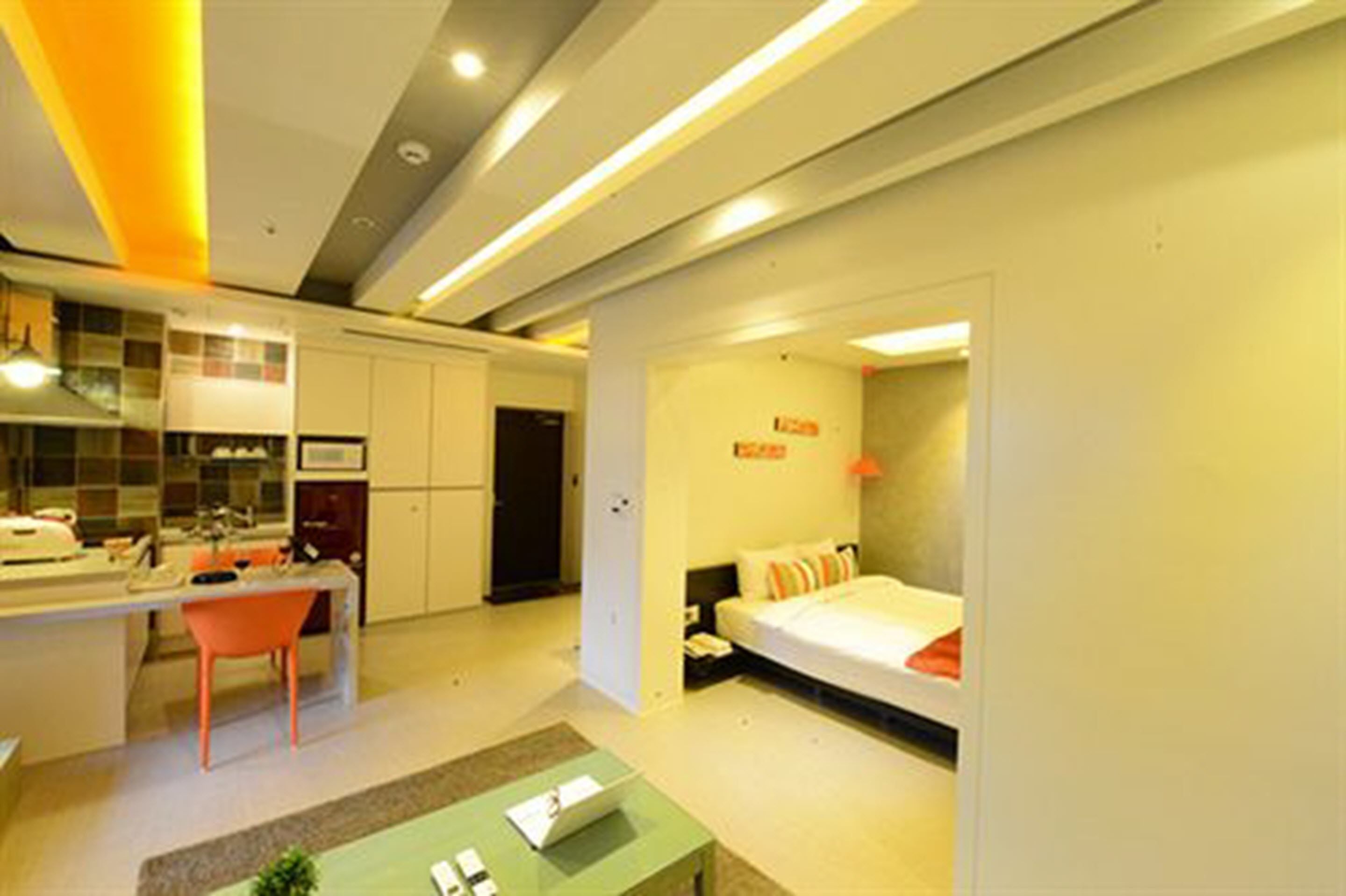 A compact hotel room with a kitchenette, a bed, and a small sitting area.