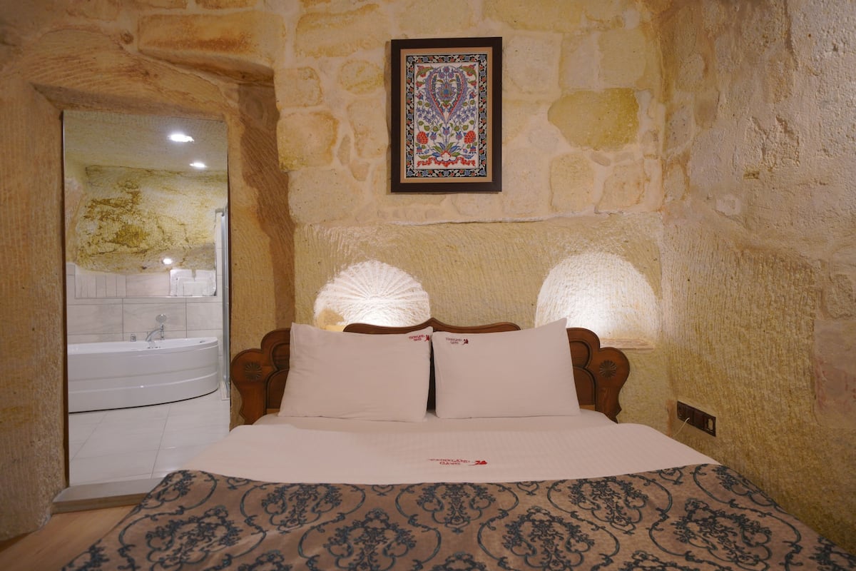 A bedroom with a stone wall, a framed artwork, a bed with two pillows, and a bathroom with a sink and bathtub.
