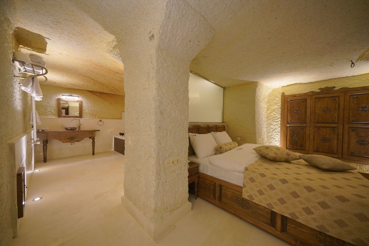A bedroom with a wooden bed, a nightstand, a mirror, and a small table with a towel rack.