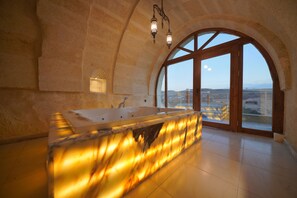 Un baño espacioso con una bañera grande, una pared de piedra y vistas a través de un amplio ventanal.