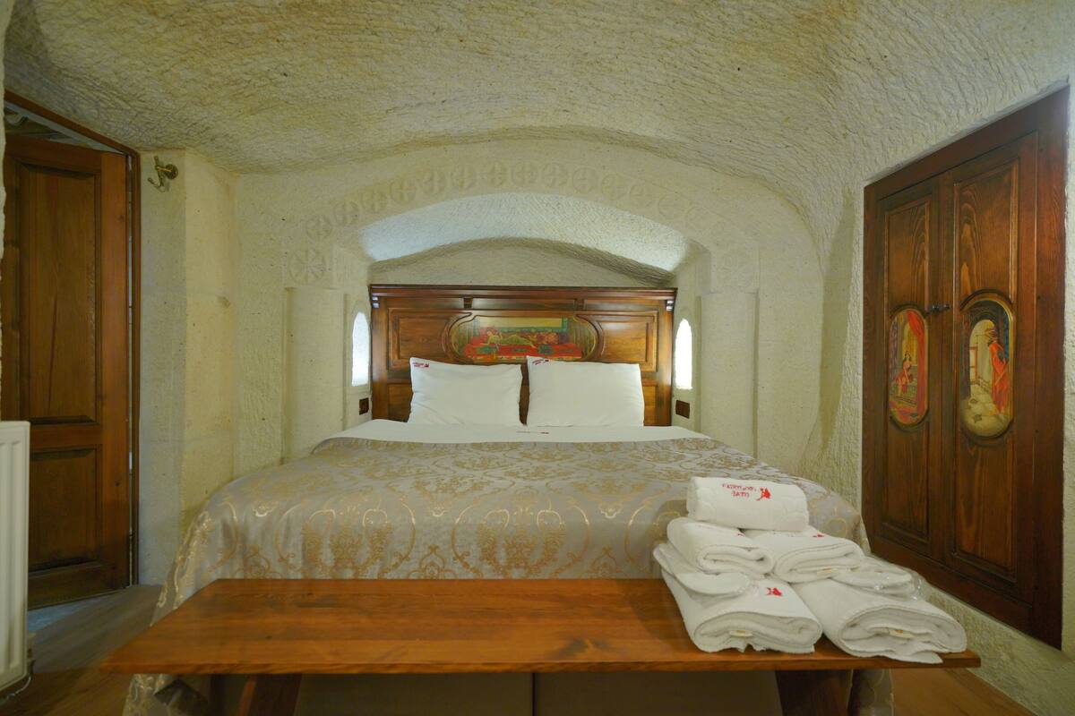 A hotel room with a bed, wooden headboard, and a table with folded towels.