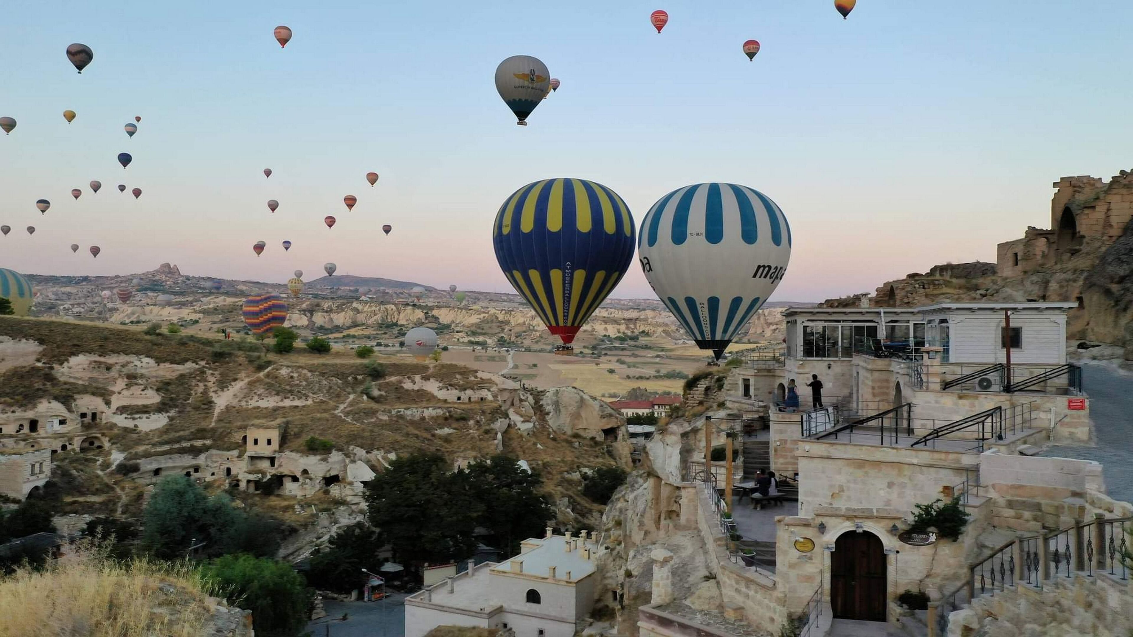 Un pueblo histórico con edificios de piedra y vistas de globos aerostáticos en el cielo.