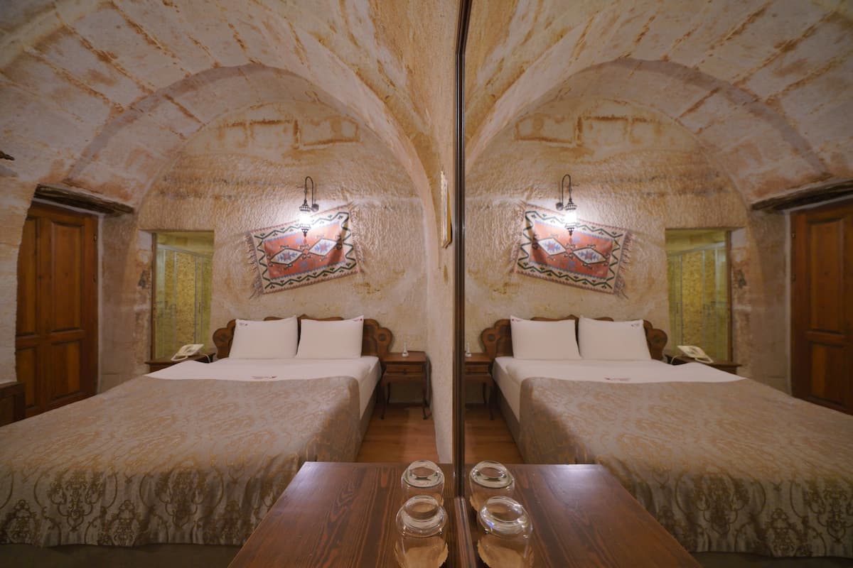 A mirrored room with two beds, wooden furniture, and a decorative wall piece.
