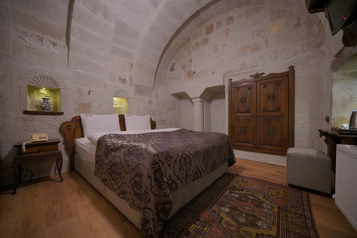 A bedroom with a bed, nightstand, wooden wardrobe, and a patterned rug.