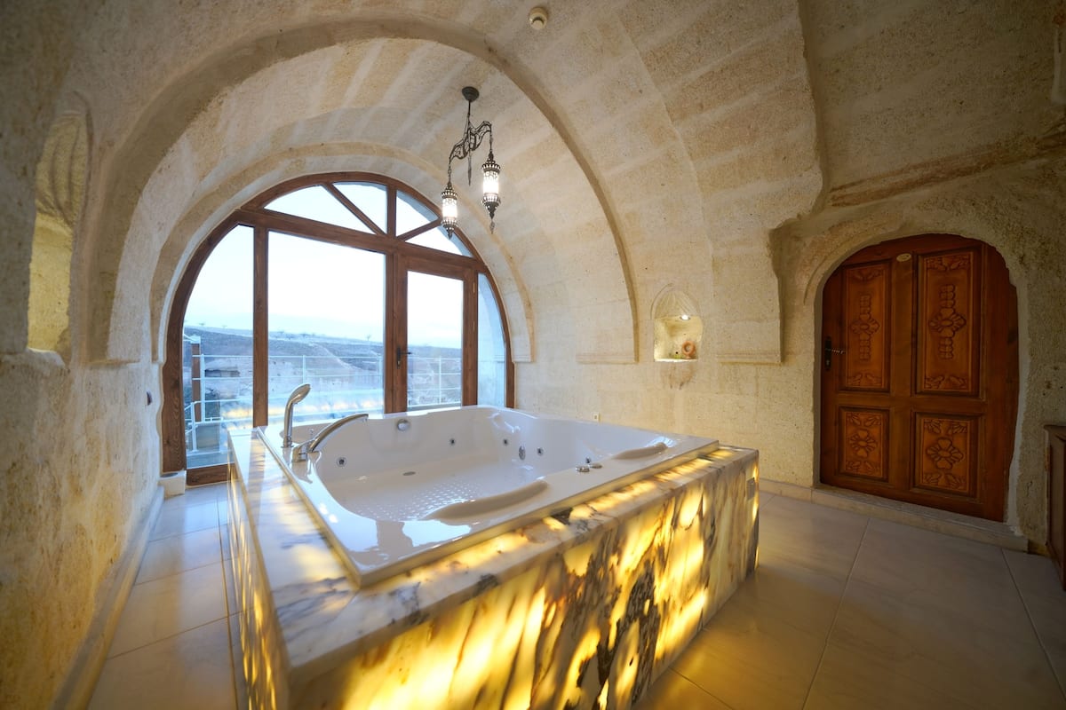 A spacious bathroom with a large bathtub, a window with a view, and a wooden door.