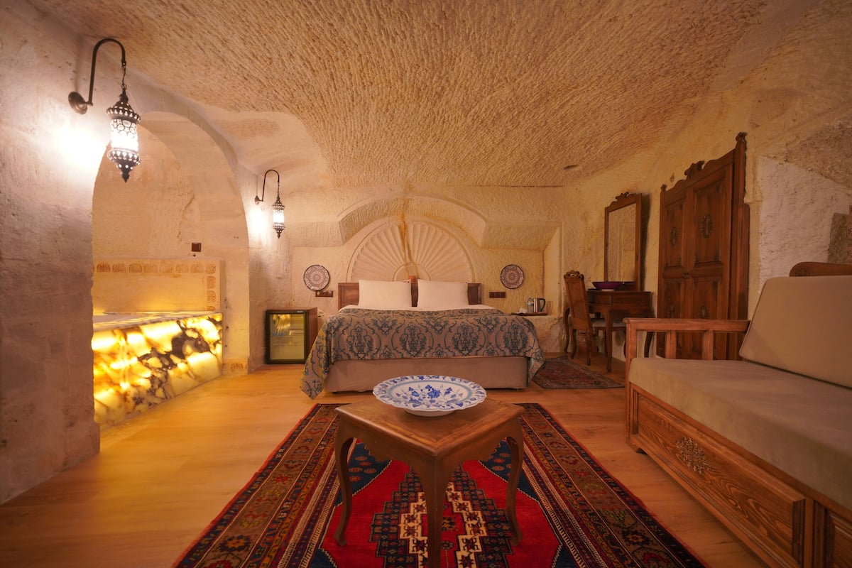A cozy bedroom with a large bed, a wooden dresser, a nightstand, and a small table with a decorative bowl.