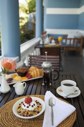 A breakfast setting with a plate of granola, yogurt, and berries, a coffee cup, and a sugar bowl on a wooden table.