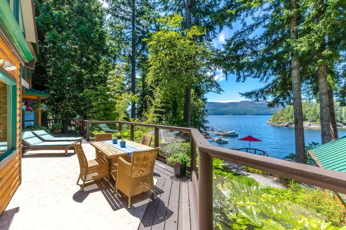 A wooden deck with wicker furniture, overlooking a lake with boats and surrounded by trees.