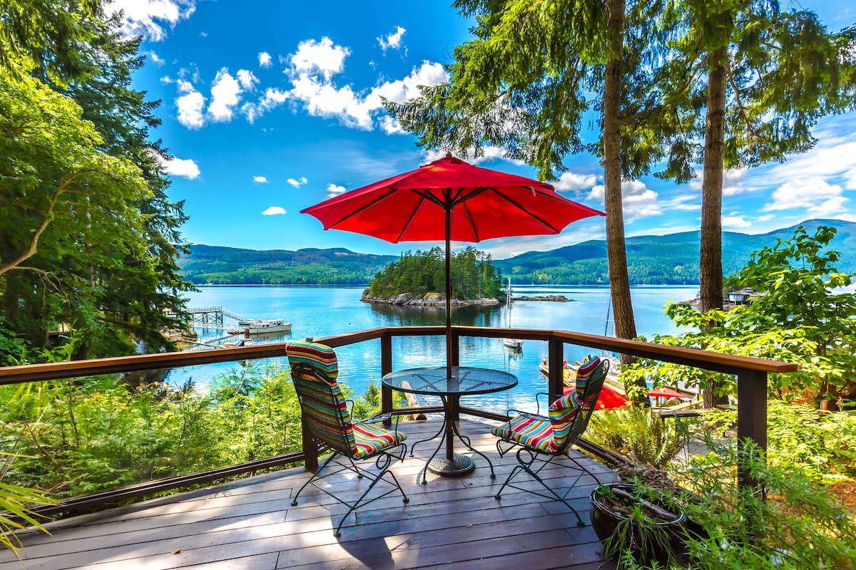 A deck with a table and chairs, overlooking a lake and a dock.