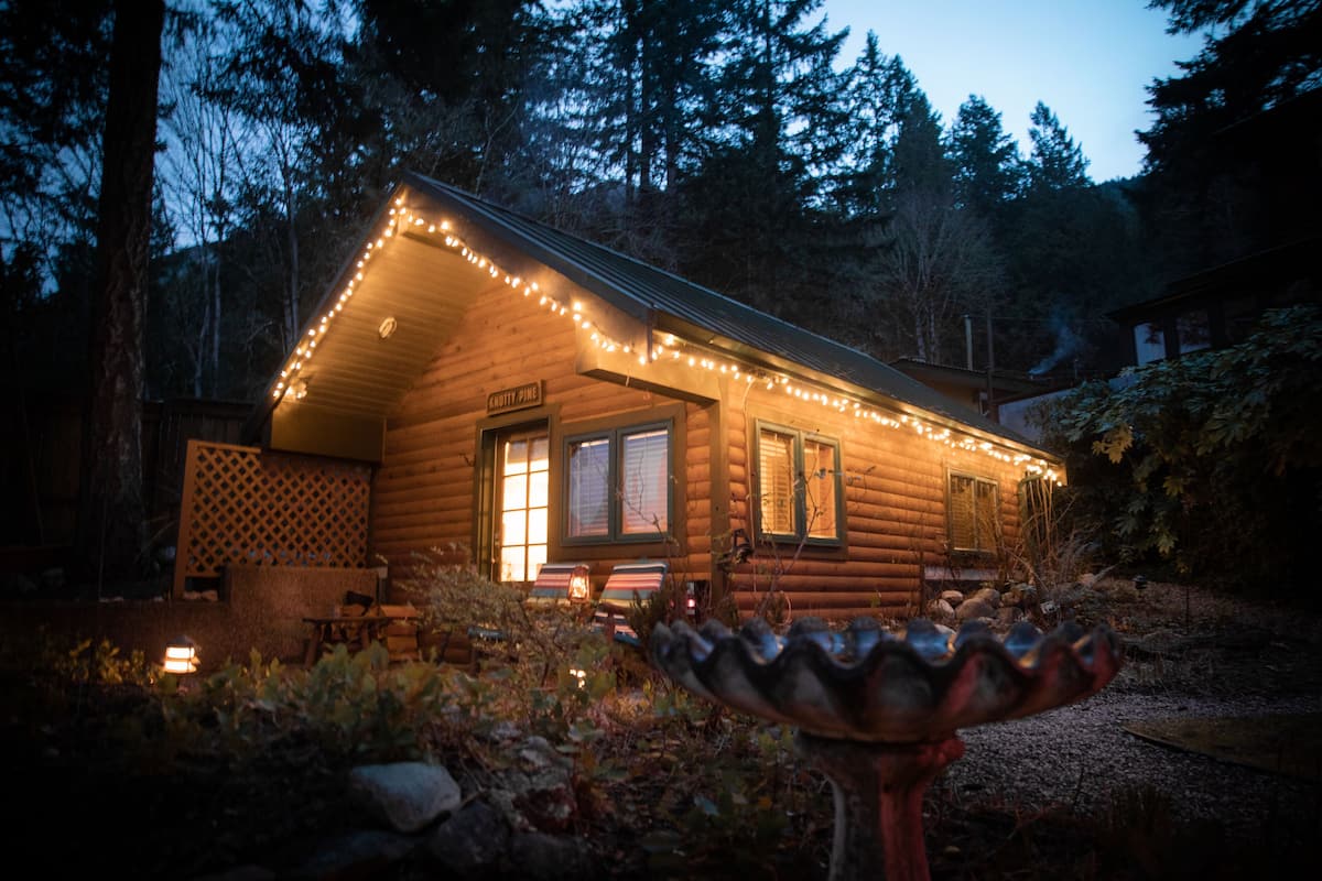 A log cabin with a porch, string lights, and a sign that reads "COTTY PINE".