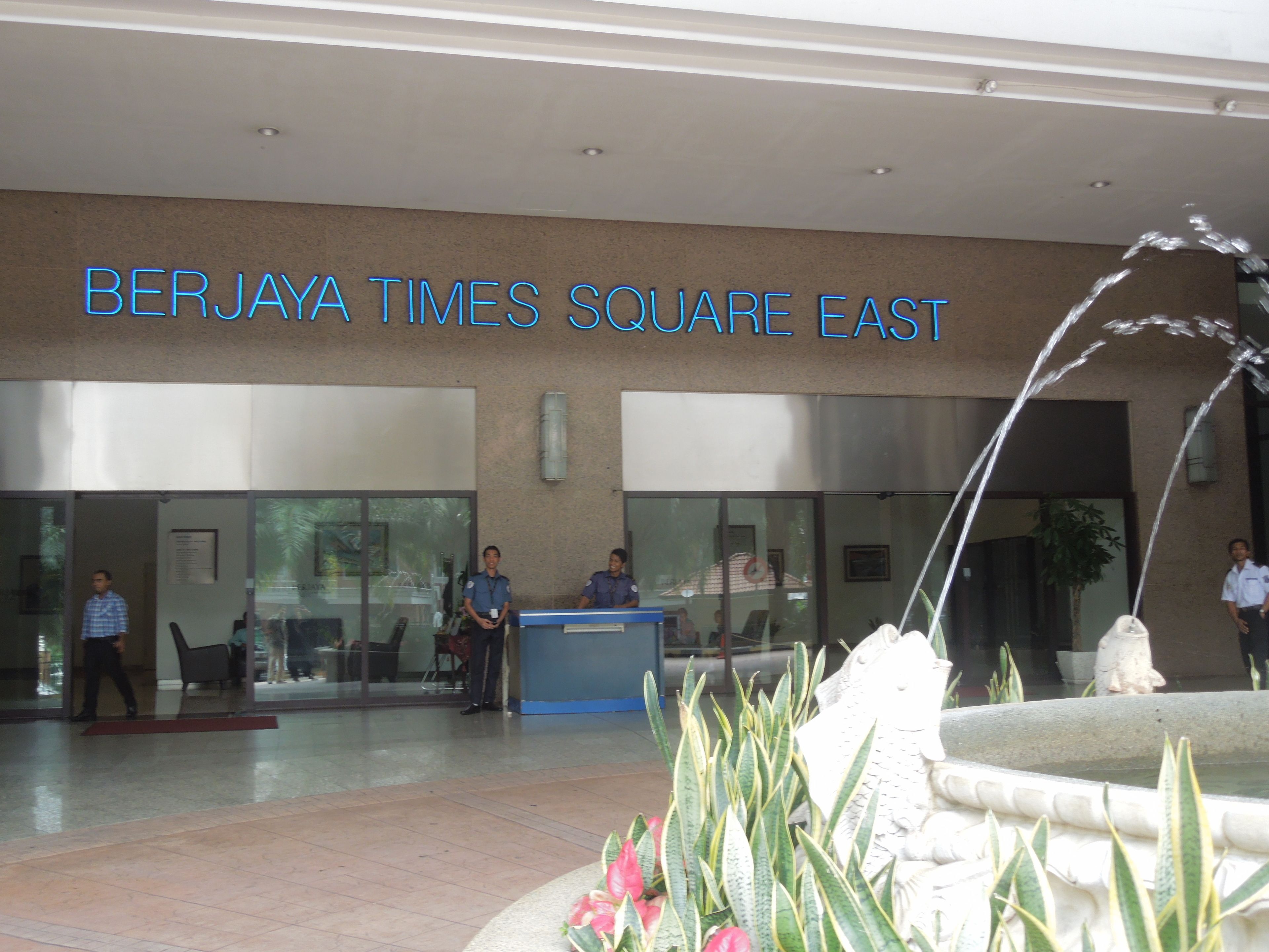 The exterior of the Berjaya Times Square East building with a reception desk, a fountain, and a few people standing outside.