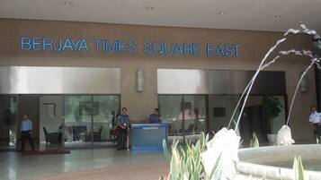 The exterior of the Berjaya Times Square East building with a reception desk, a fountain, and a few people standing outside.