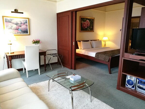 A hotel room with a bed, a desk, a chair, a glass table, a TV, and a painting on the wall. - Times Private Serviced Suites (Kuala Lumpur)