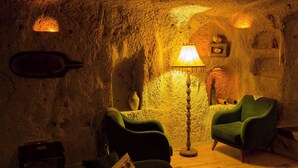 Un interior rústico con paredes de piedra, un sillón verde, una lámpara de pie y una mesita.