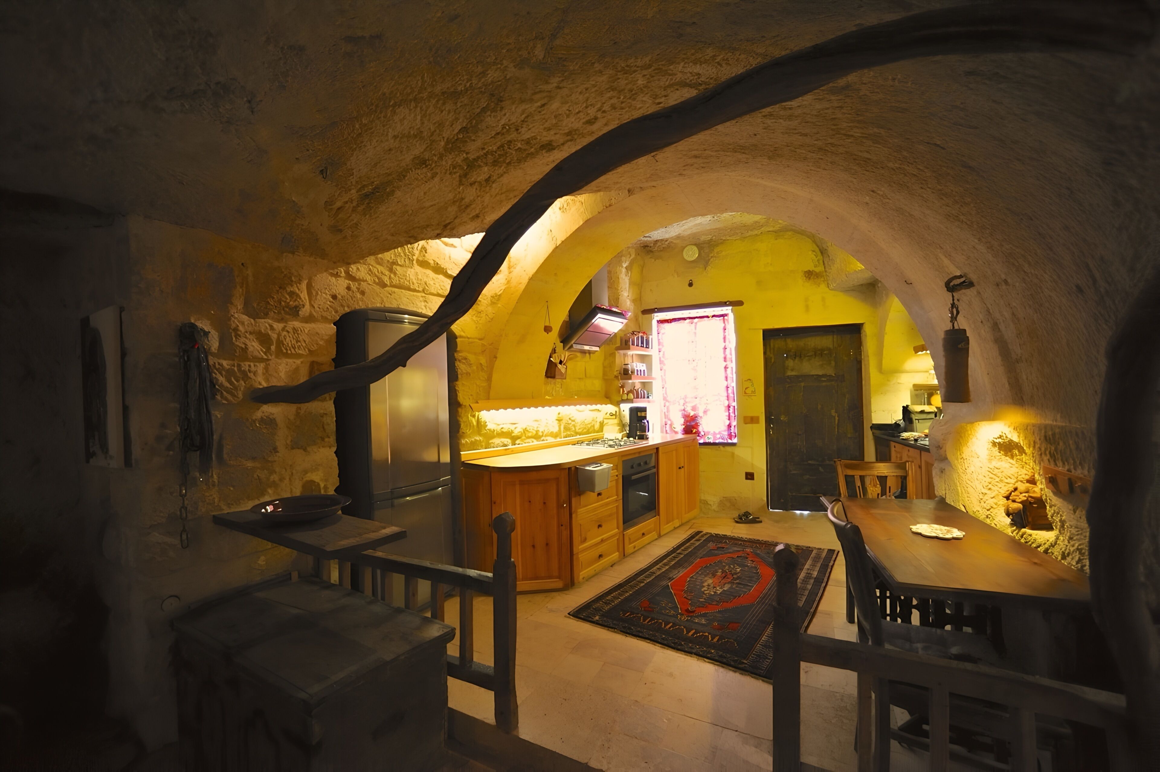 A rustic stone interior with a kitchen, dining area, and a wooden staircase.