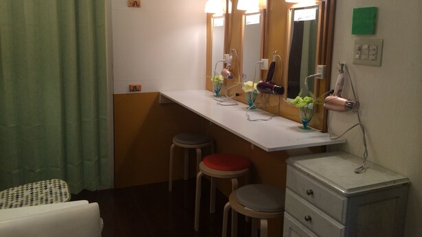 A bathroom with a vanity, two stools, a mirror with lights, a toilet sign, and a small green sign on the wall. - SAKURA GUEST HOUSE OSAKA DOUTONBORI - Hostel (Osaka)