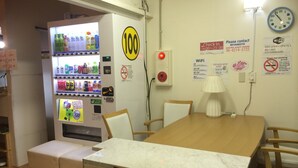 A room with a wooden table, white chairs, a vending machine, and various signs including a Wi-Fi sign, a clock, and a no-smoking sign. - SAKURA GUEST HOUSE OSAKA DOUTONBORI - Hostel (Osaka)
