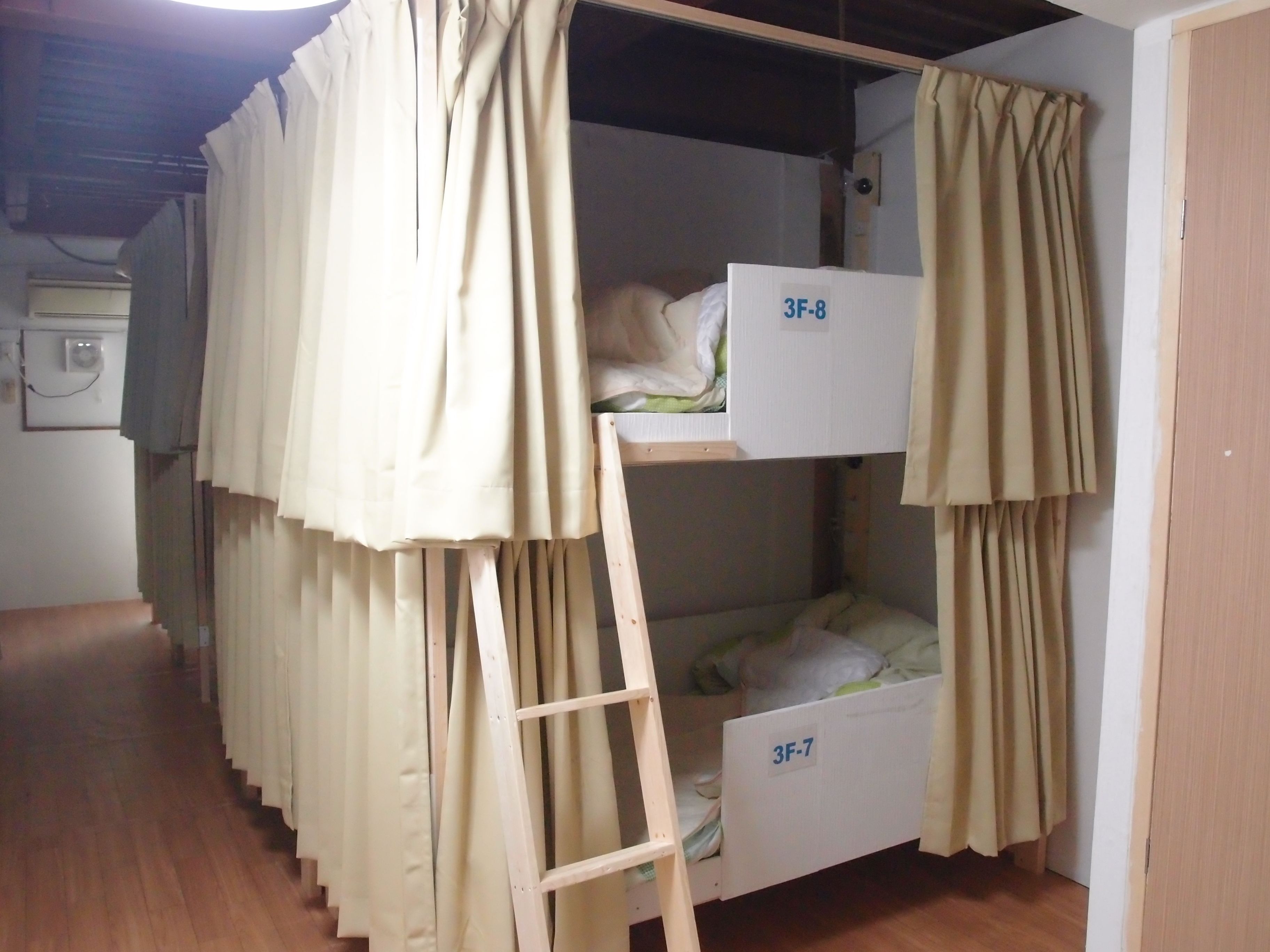 Quarto com beliche, cortinas, escada e ar condicionado fixado na parede.