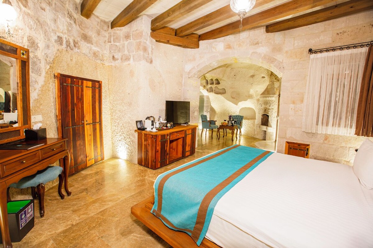A bedroom with a bed, wooden desk, television, and stone walls.