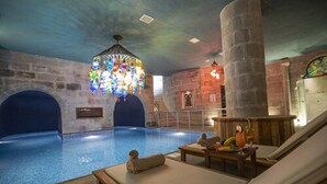 A swimming pool area with lounge chairs, a colorful chandelier, and stone walls.
