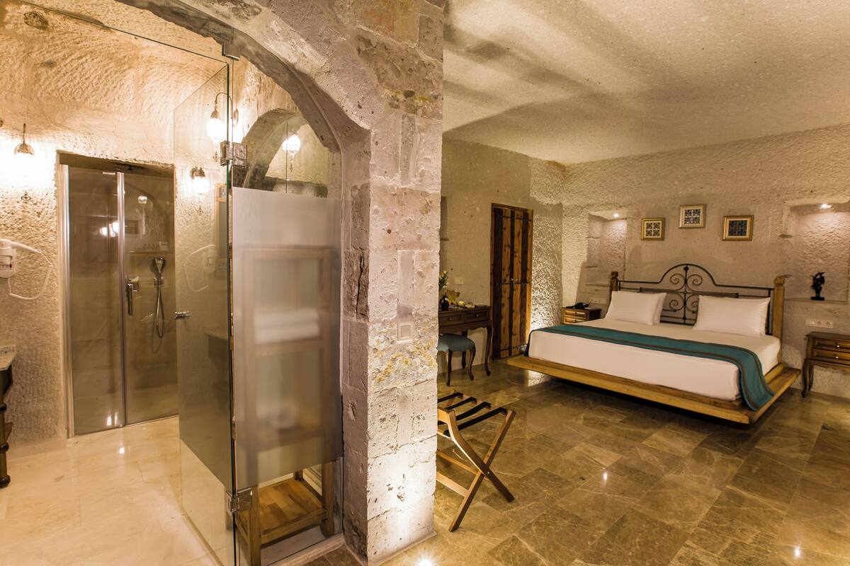 A bedroom with a large bed, a wooden chair, a nightstand, and a glass shower enclosure.