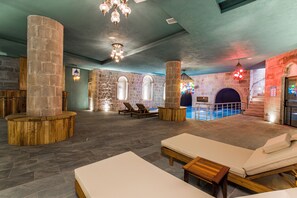 A spa area with stone pillars, lounge chairs, and a pool.