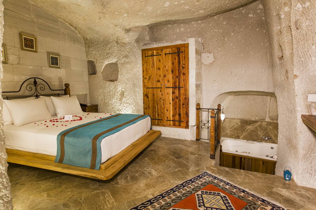 A bedroom with a bed, a wooden door, a bathtub, and a patterned rug.